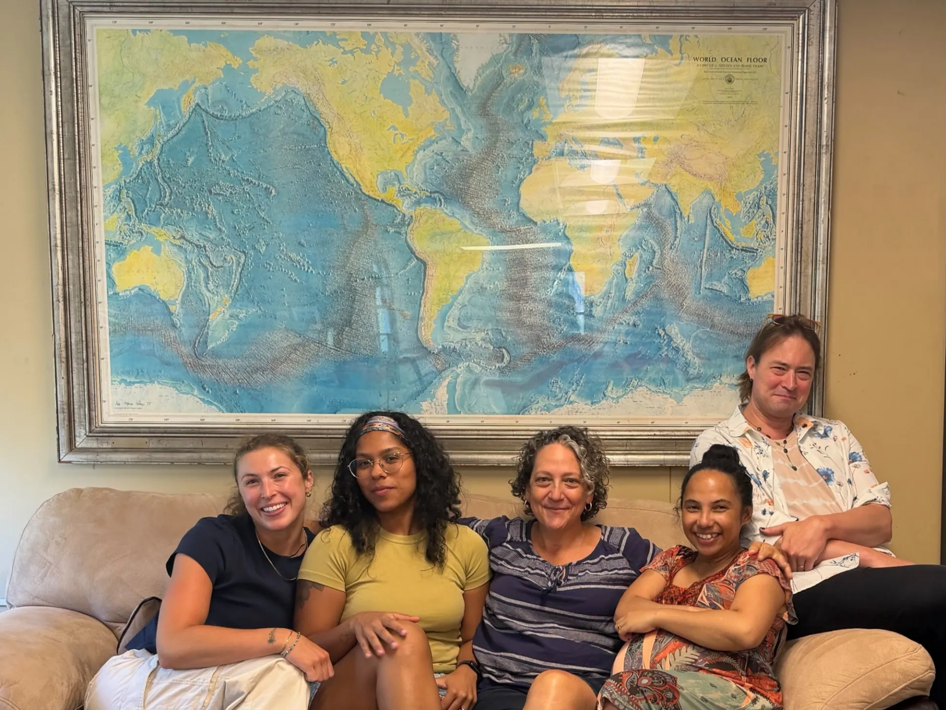 Vicki Ferrini and her team sitting on a couch under a copy of the 1977 World Ocean map